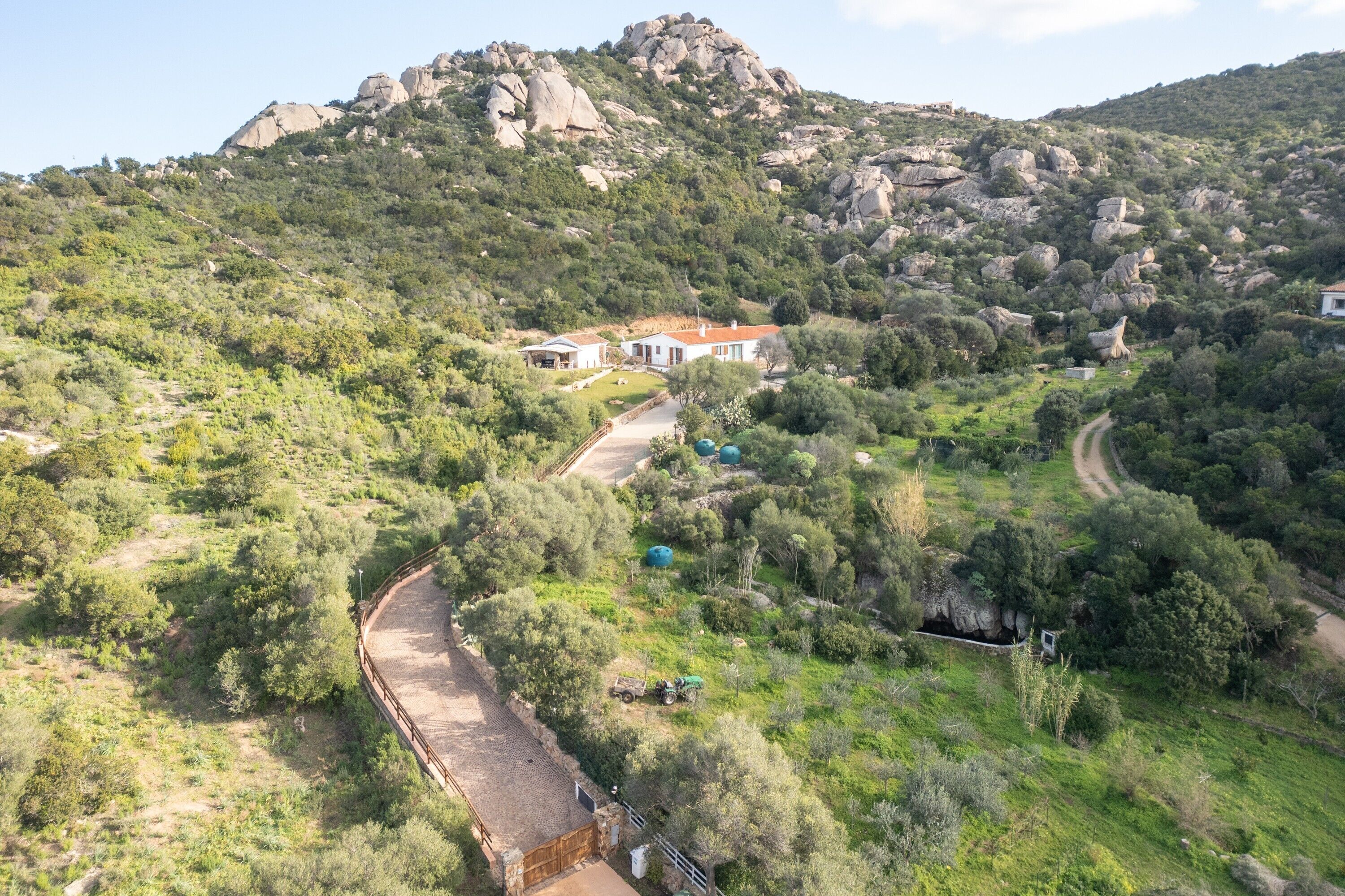 A rural landscape with a house surrounded by greenery and rocky terrain.