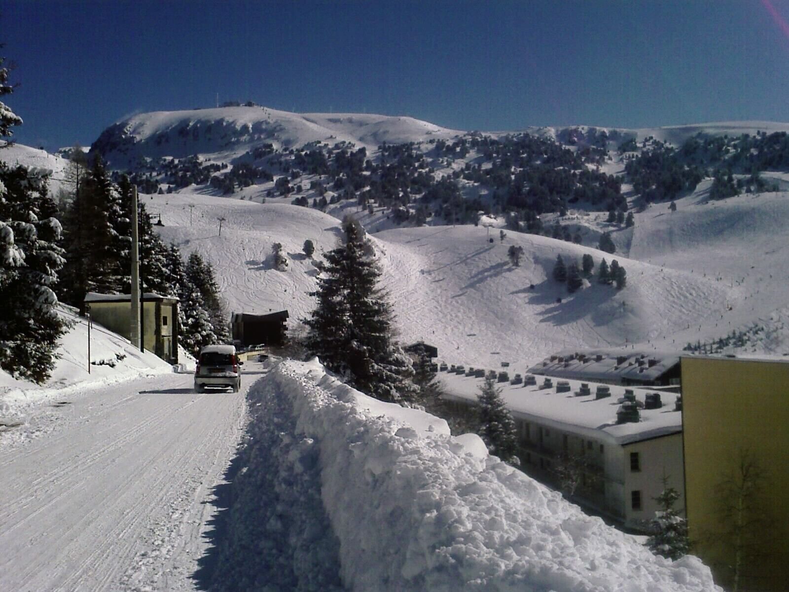 A snow-covered road with a vehicle, buildings, and a mountainous landscape in the background.