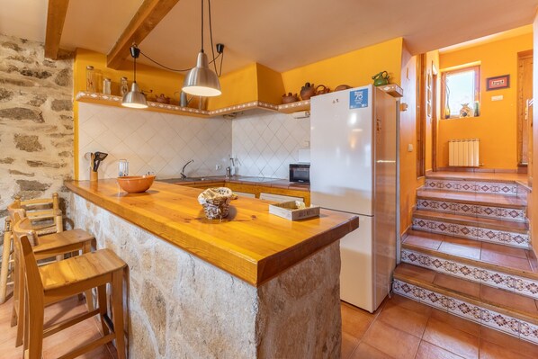 A kitchen with a wooden island, a refrigerator, and a stone wall.