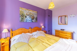 A bedroom with a wooden bed, two bedside lamps, a dresser, a mirror, and a painting on the wall. - Casa del Tio Primitivo – Rural House with Mountain Views in Ávila (Navarredonda De Gredos)