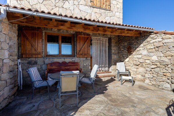 Un bâtiment en pierre doté d’un balcon en bois, d’un espace extérieur aménagé pour s’asseoir et d’un mur en pierre.