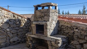 A stone-built outdoor structure with a chimney, possibly a fireplace or oven, surrounded by stone walls and a tiled roof.