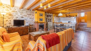 A cozy living room with a fireplace, wooden beams, and a stone wall.