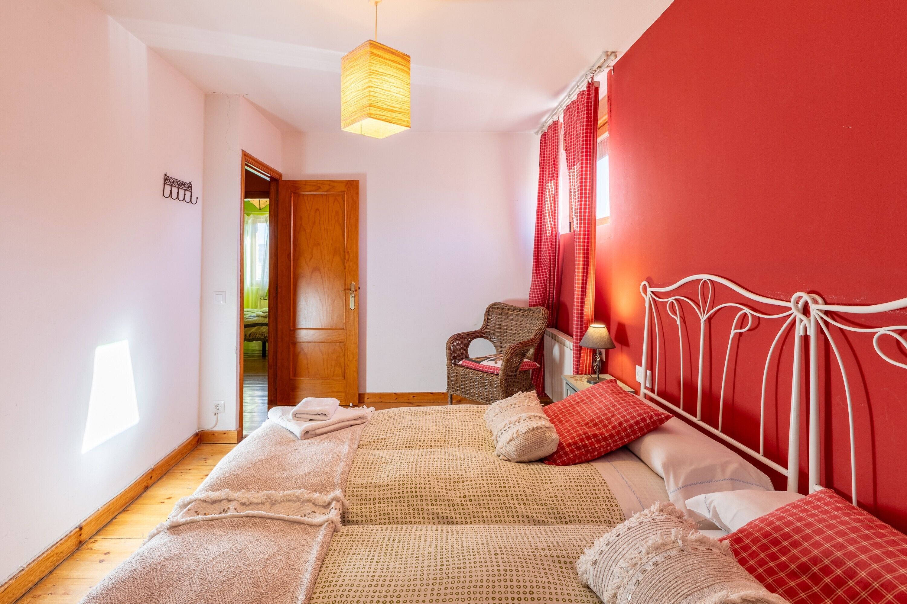 Un dormitorio con cama, una silla, una lámpara colgante y una puerta que da a otra habitación.