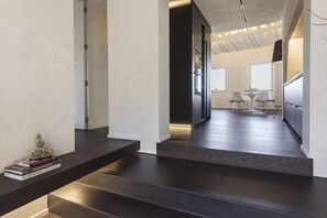A modern interior with a staircase, a dining area with chairs and a table, and a kitchen area with cabinets and a refrigerator.
