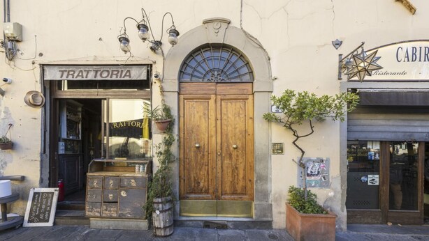 Ein Gebäude mit einer Holztür, einem Schild mit der Aufschrift 'TRATTORIA' und einem weiteren Schild für 'CABIR'.