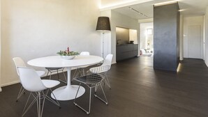 Ein moderner Essbereich mit einem runden Tisch, weißen Stühlen, einer Stehlampe und einer Küche im Hintergrund.