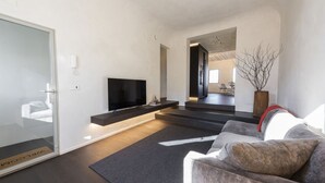 Ein modernes Wohnzimmer mit Flachbildfernseher, einer Couch, einem Couchtisch und minimalistischem Design.