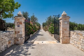 Ein gepflasterter Weg führt zu einem verschlossenen Eingang mit steinernen Säulen und blauem Himmel.