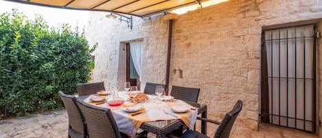 An outdoor dining area with a table set for four, surrounded by wicker chairs, under a canopy.