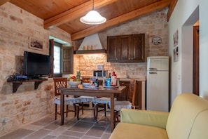 Un'accogliente cucina con parete in pietra, mobili in legno, un tavolo da pranzo con sedie, un televisore e un frigorifero.