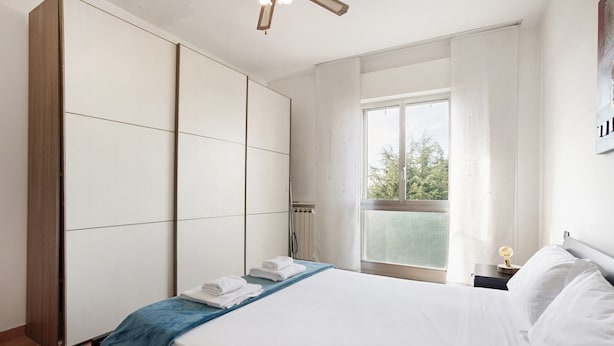 Een hotelkamer met een bed, een raam met uitzicht, een nachtkastje en een kledingkast.