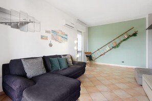 A living room with a sectional sofa, a staircase with a wooden handrail, and a wall-mounted air conditioning unit.