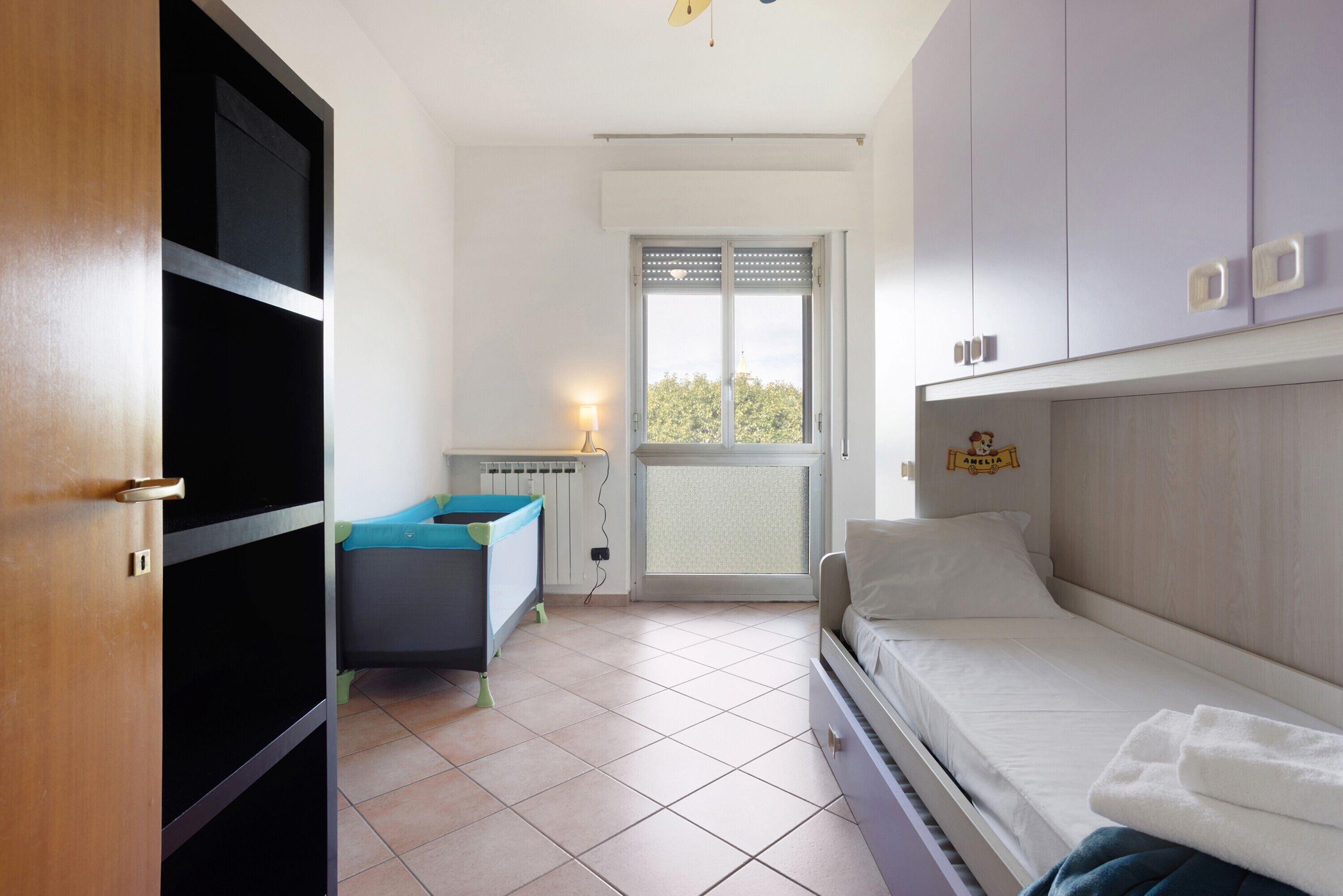 Una stanza con un letto, una scrivania, un termosifone, una finestra e una porta.
