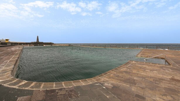 Una amplia piscina al aire libre con solárium de piedra, una construcción pequeña y vistas al mar.