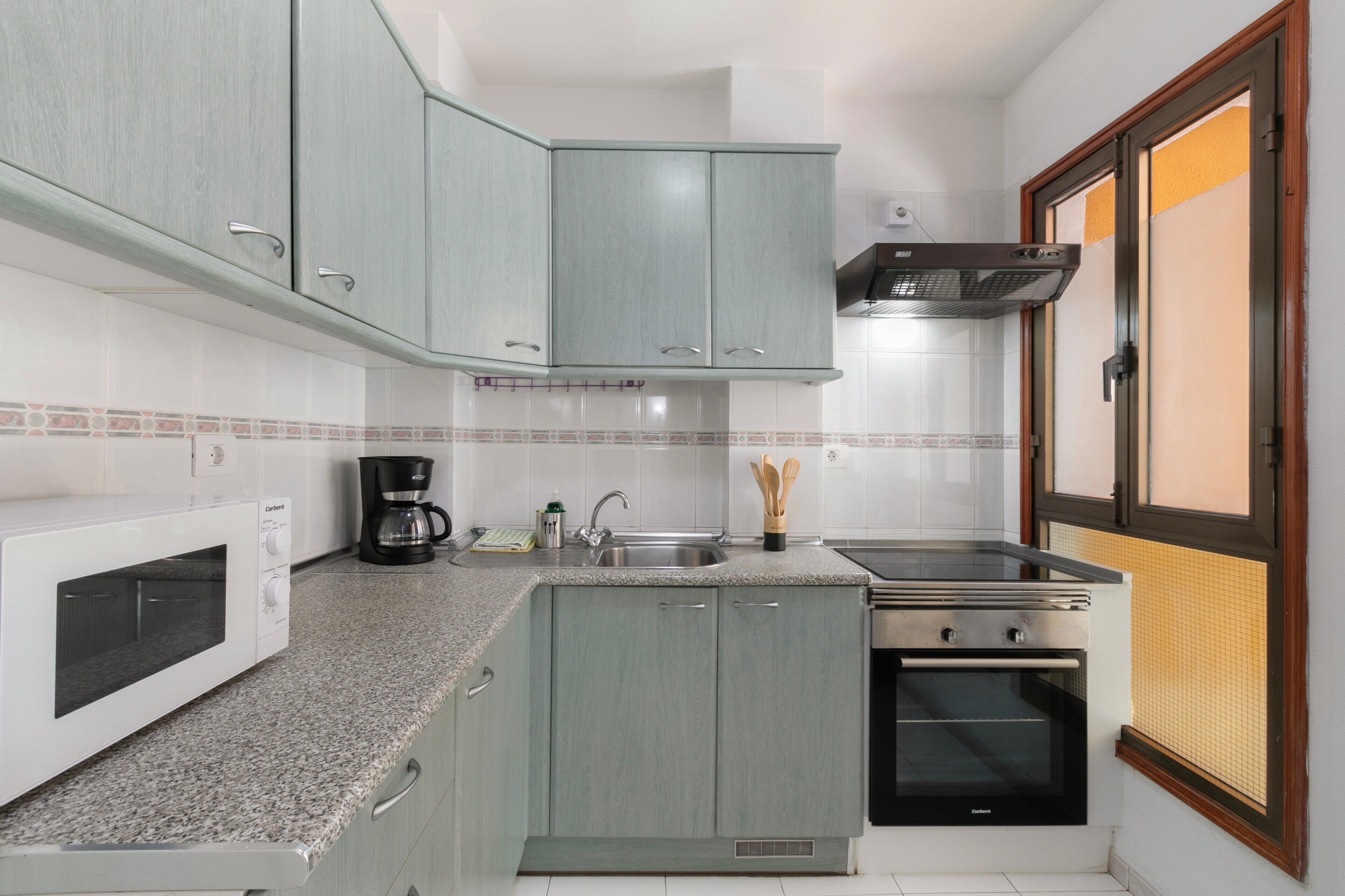 A kitchen with a microwave, coffee maker, sink, stove, and cabinets.