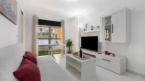 Una sala de estar moderna con un sofá, televisor, mesa de centro y un área de comedor visible a través de un vidrio.