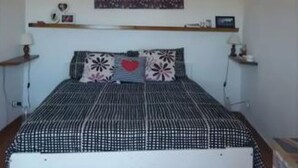 A bedroom with a bed, a wall-mounted shelf, and a decorative piece above the bed.