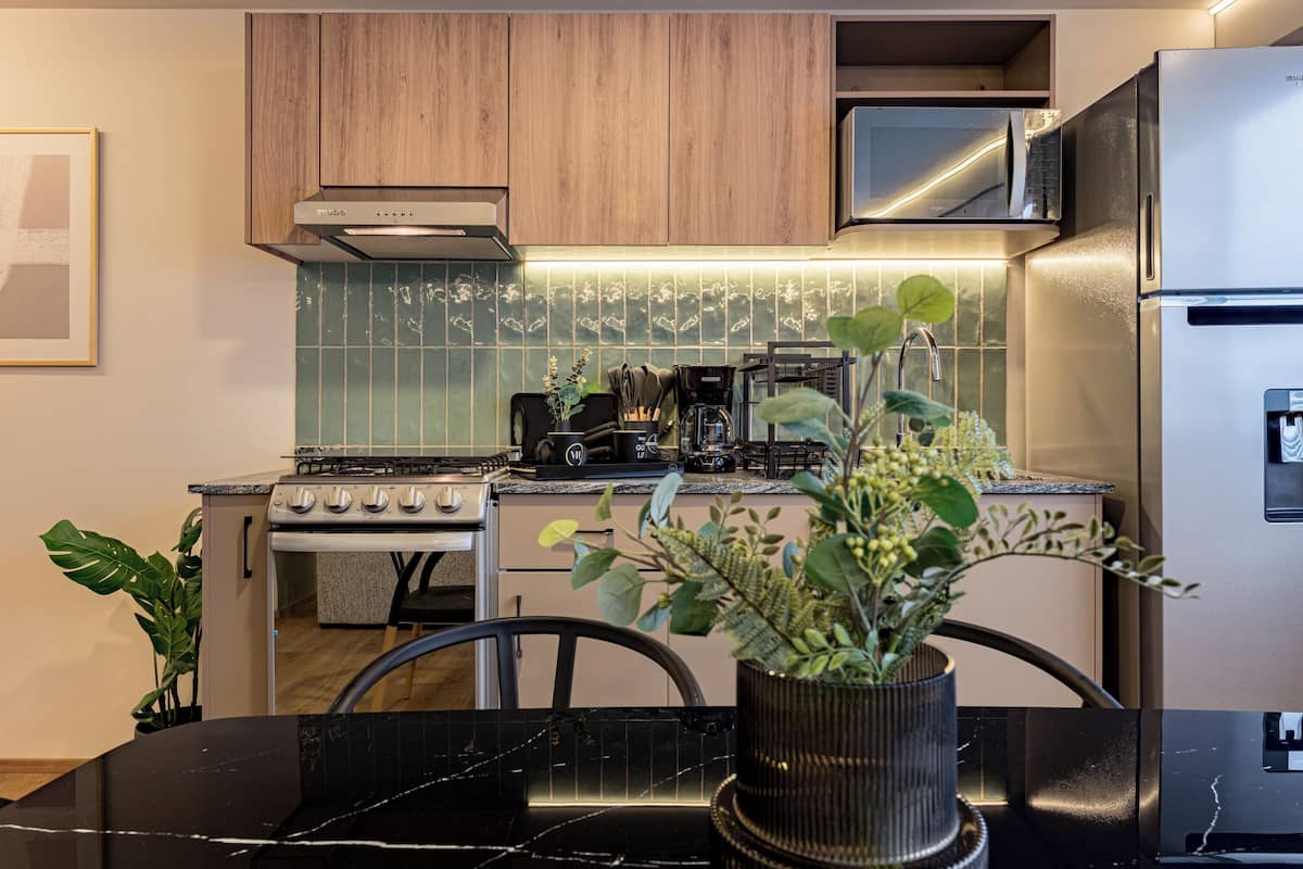 A modern kitchen with a stove, oven, microwave, and refrigerator. There is a dining table with chairs and a potted plant.