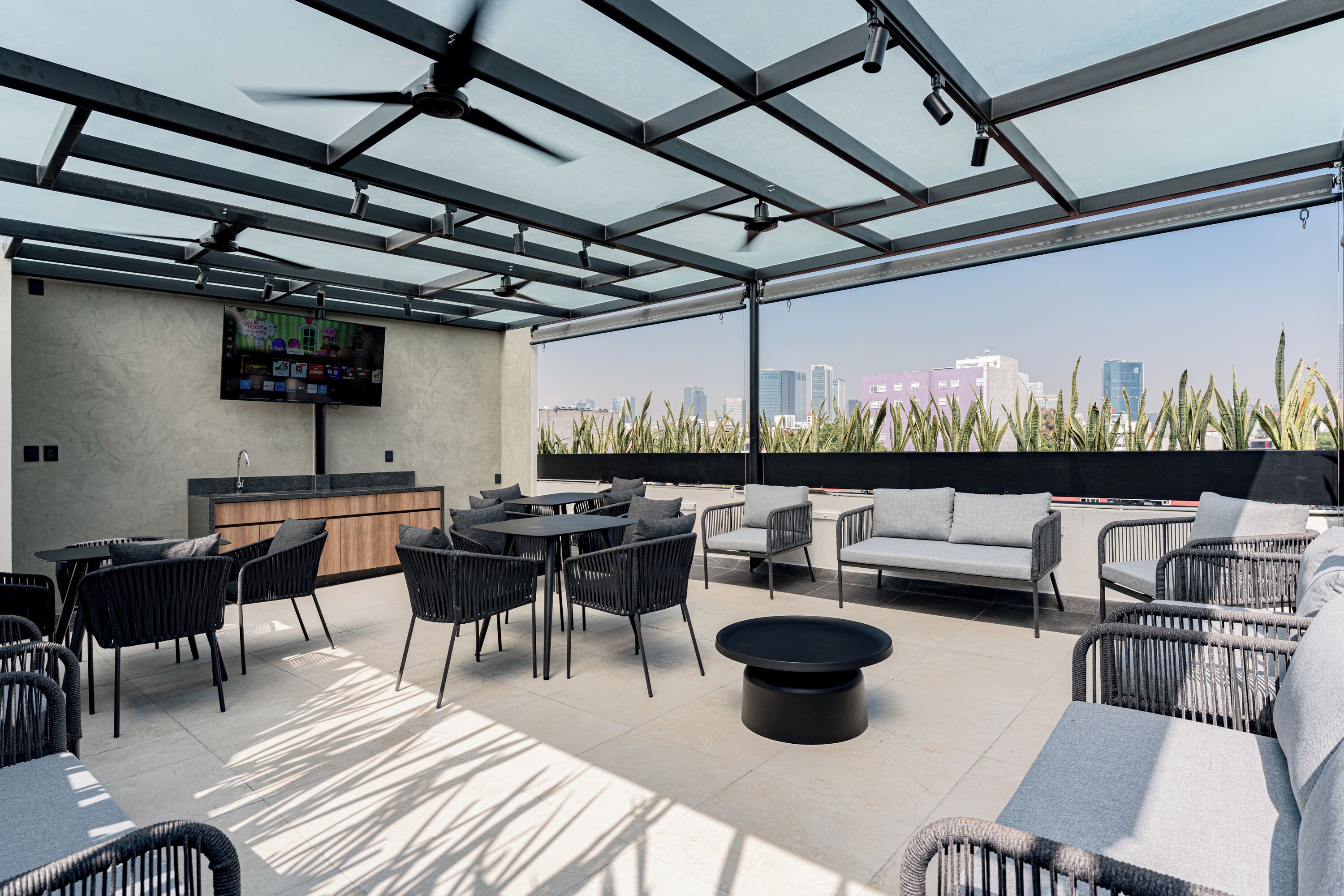 A rooftop bar with a city view, featuring a bar area, seating, and a TV screen.