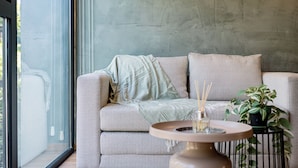 A modern living room with a grey sofa, a round table with a vase, and a potted plant. - Mint Roma Residences (Mexico City)
