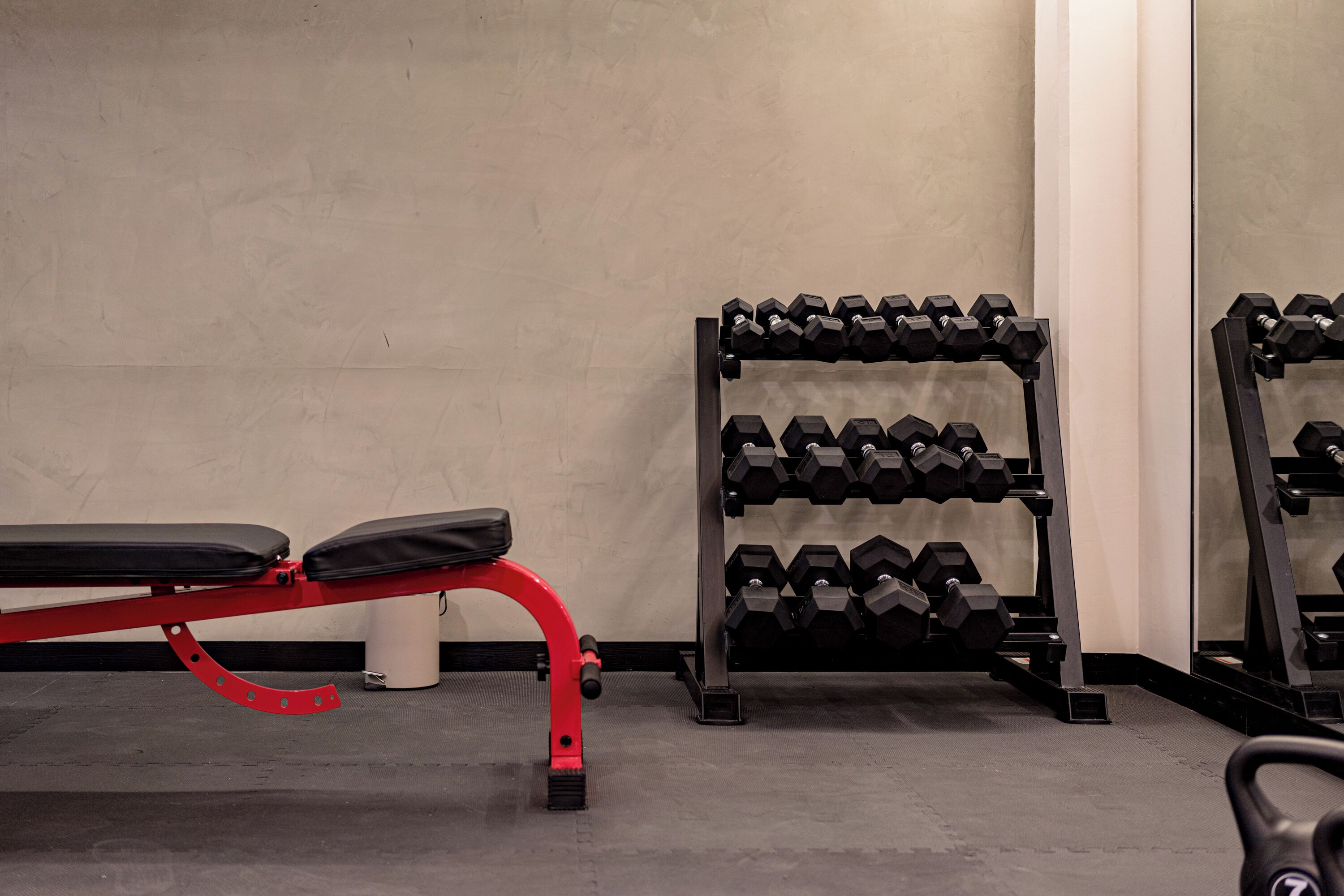 Une salle de sport équipée d’un banc, d’haltères et d’un tapis de course.