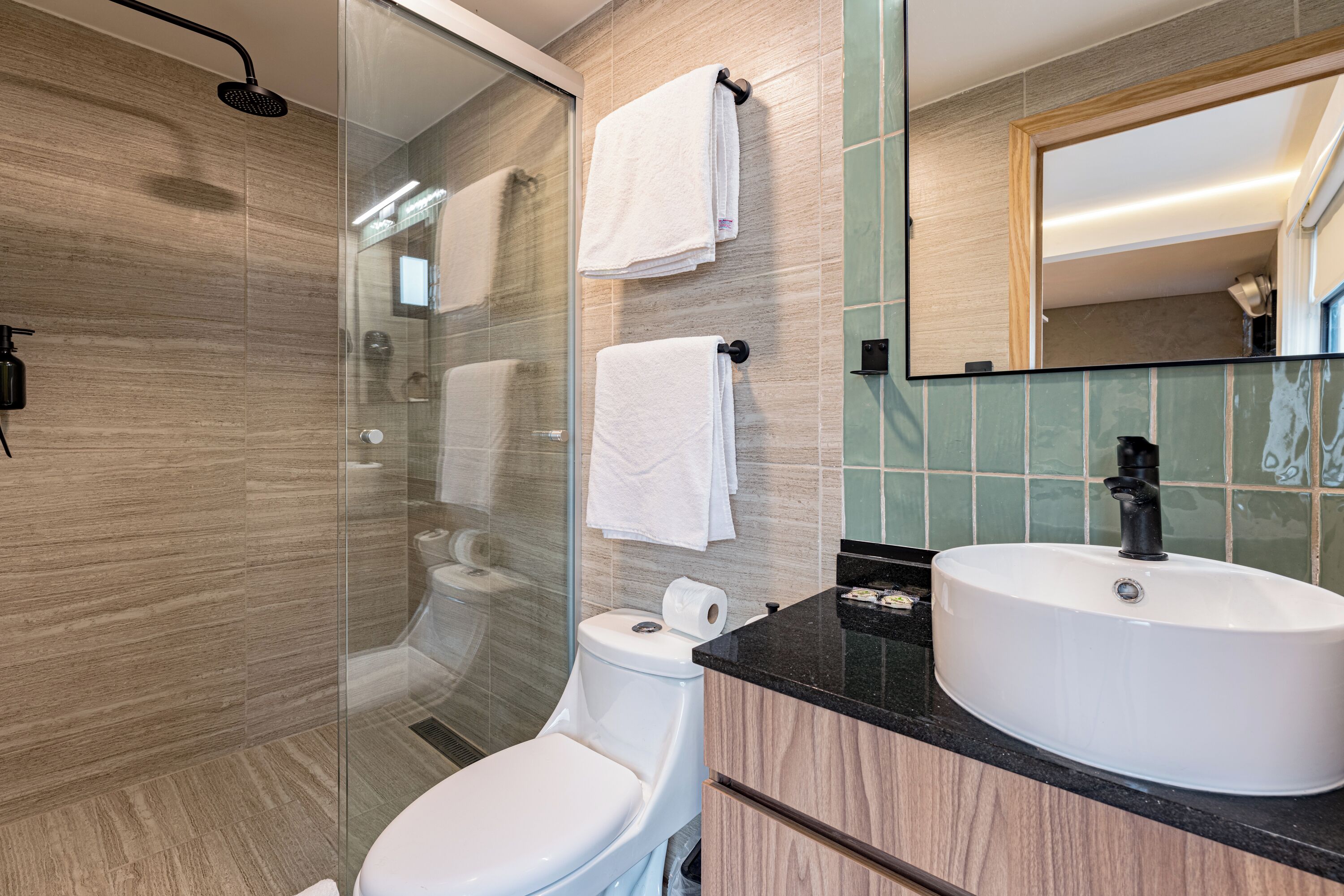 A modern bathroom with a glass-enclosed shower, a white toilet, and a vanity with a large sink and mirror.