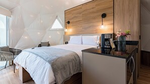 A modern bedroom with a large bed, a wooden headboard, a small kitchenette, and a geometric ceiling design. - Mint Roma Residences (Mexico City)