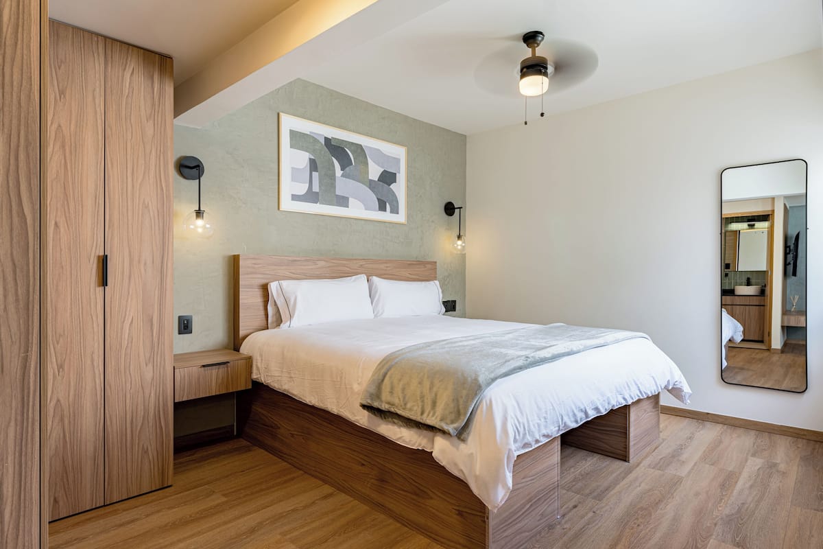 A bedroom with a wooden bed, a nightstand, a wall-mounted light, and a mirror.