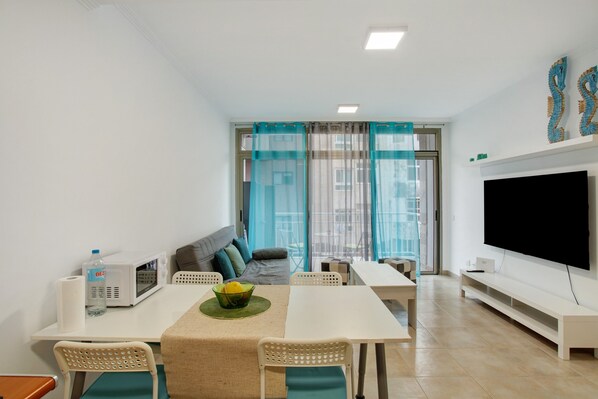 A modern living room with a dining area, a flat-screen TV, and a sofa.