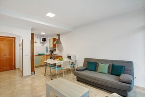 A compact living space with a kitchenette, a dining area, and a sofa with cushions.