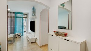 Ein modernes Wohnzimmer mit einem Flachbildfernseher, einer dekorativen Schale auf einem weißen Schrank und einem großen Spiegel an der Wand.