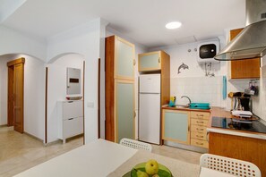 A compact kitchen with a refrigerator, stove, and wooden cabinets.