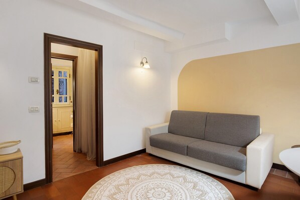 Una sala de estar con un sofá gris, un tapete estampado y una puerta que da a la cocina.