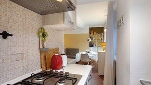 A kitchen with a gas stove, a red kettle, and a white countertop.