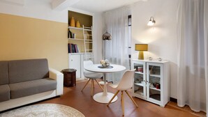 A living room with a sofa, a round table with chairs, a bookshelf, a cabinet with glass doors, and a lamp.