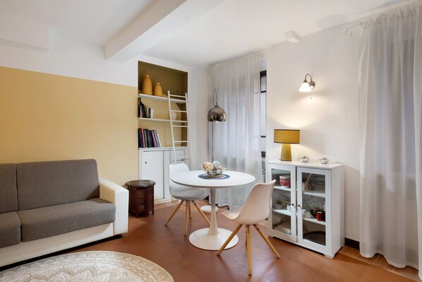 A living room with a sofa, a round table with chairs, a bookshelf, a cabinet with glass doors, and a lamp.