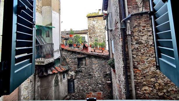 A narrow street with stone buildings, a staircase, and a metal gate.