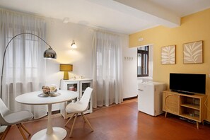 A modern living room with a round table, white chairs, a television on a wooden cabinet, and a refrigerator.