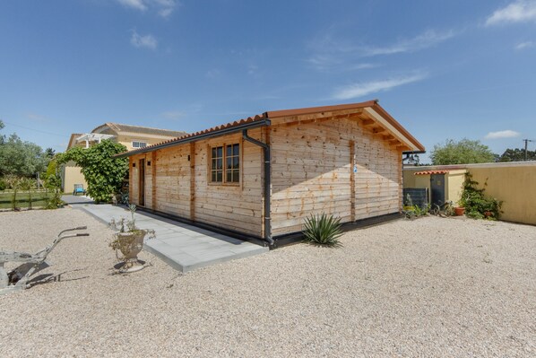 A wooden cabin with a sloped roof, a gravel driveway, and a potted plant in the foreground.
