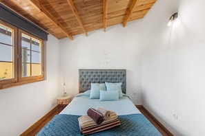 Une chambre avec un plafond en bois, un lit recouvert d’une couette bleue et une table de chevet avec une lampe.