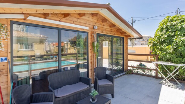 A covered outdoor seating area with wicker furniture and a table, overlooking a swimming pool.