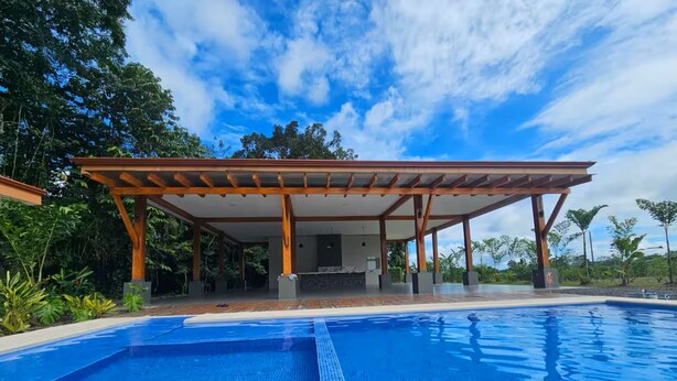 Una piscina con un patio coperto, circondata da una vegetazione rigogliosa.