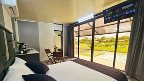 Camera d'albergo con un letto grande, una scrivania con una sedia, una TV e vista su una piscina e del verde.