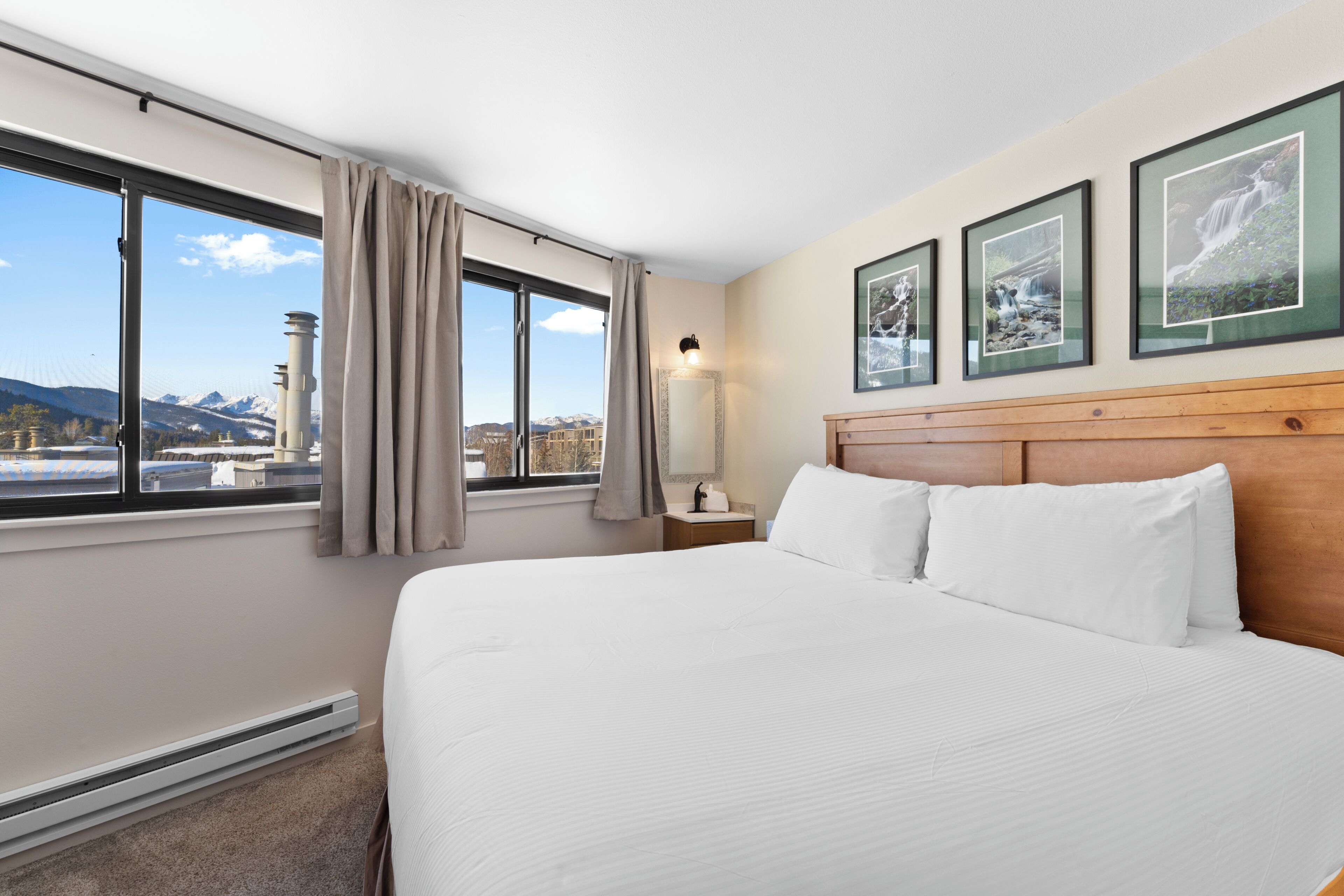 A hotel room with a large bed, a nightstand, a lamp, and a window with a view of mountains.