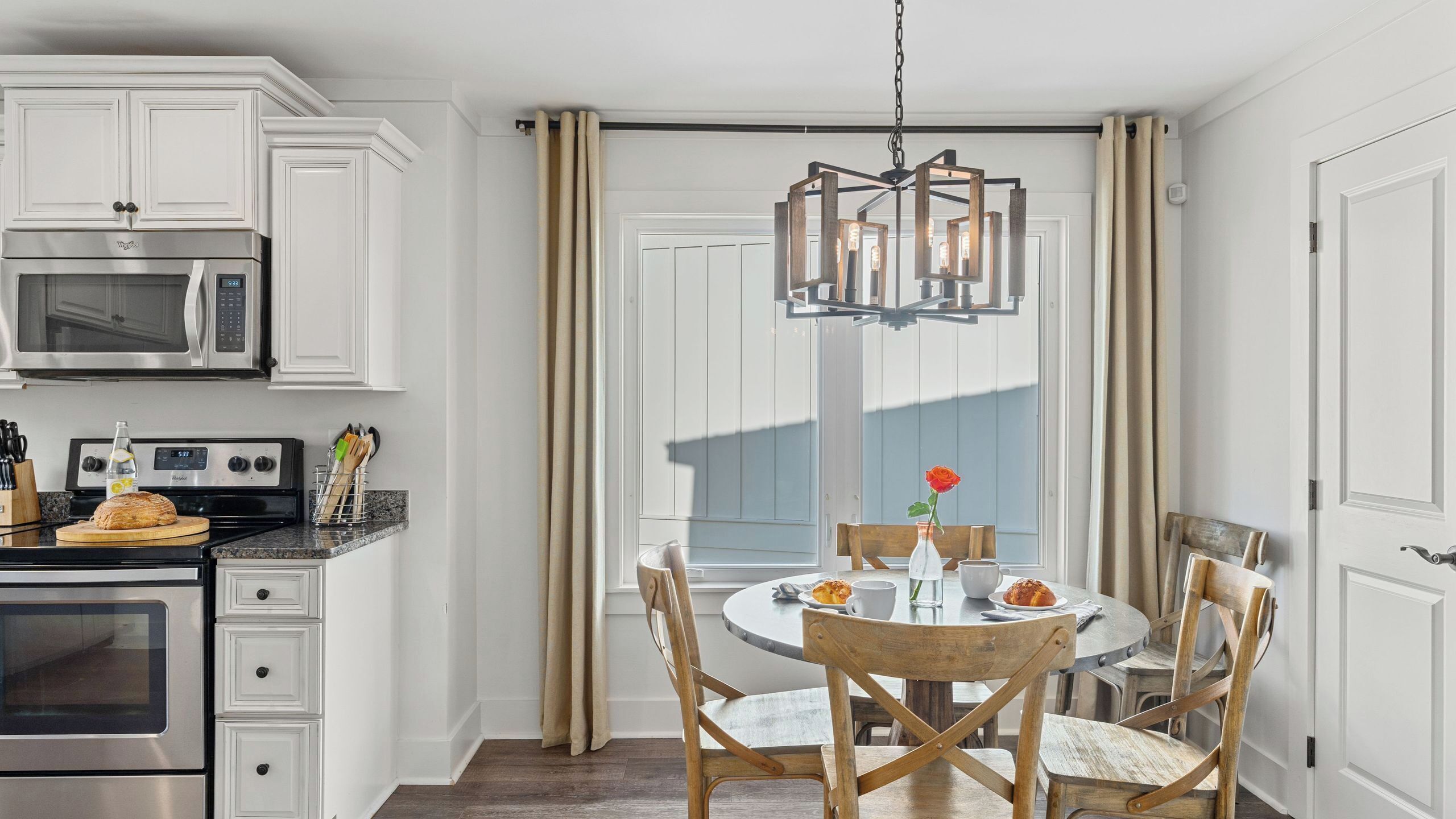 A kitchen with white cabinetry, a stainless steel stove, and a dining area with a round table and wooden chairs.