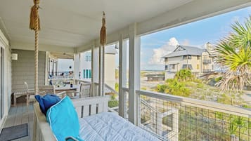 Un balcon avec vue sur la plage, un coin repas avec des meubles d’extérieur et une décoration suspendue faite de cordes.