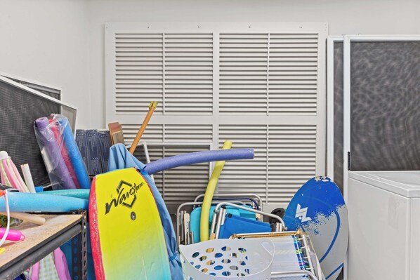 A storage area with various items including a yellow surfboard, blue and pink towels, and cleaning supplies.