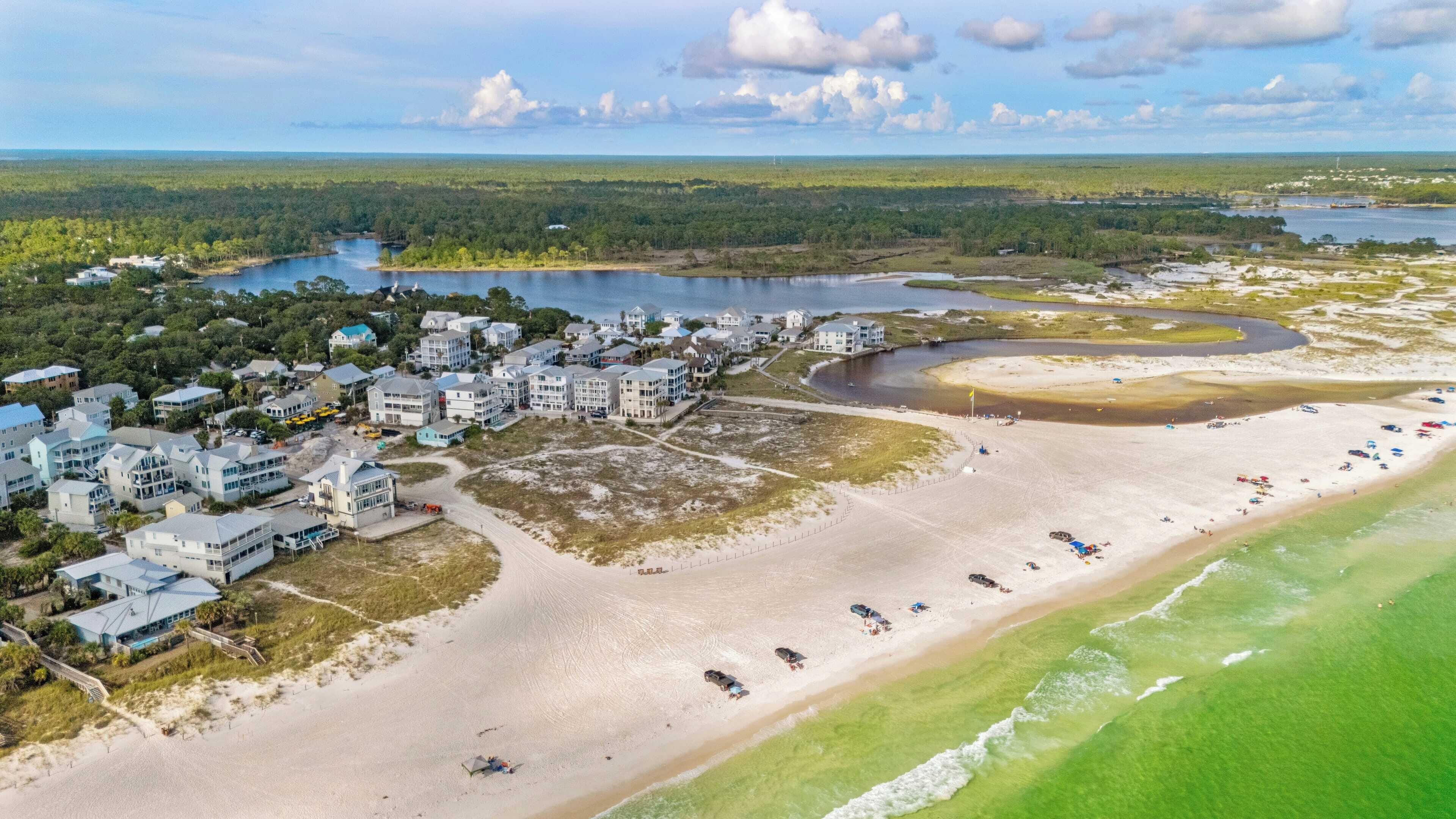 Luchtbeeld van een kustresort met strandwoningen, een zandstrand en een jachthaven.