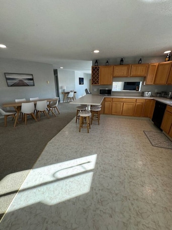 A modern kitchen with wooden cabinets, a dining area with a white table and chairs, and a large window providing natural light.